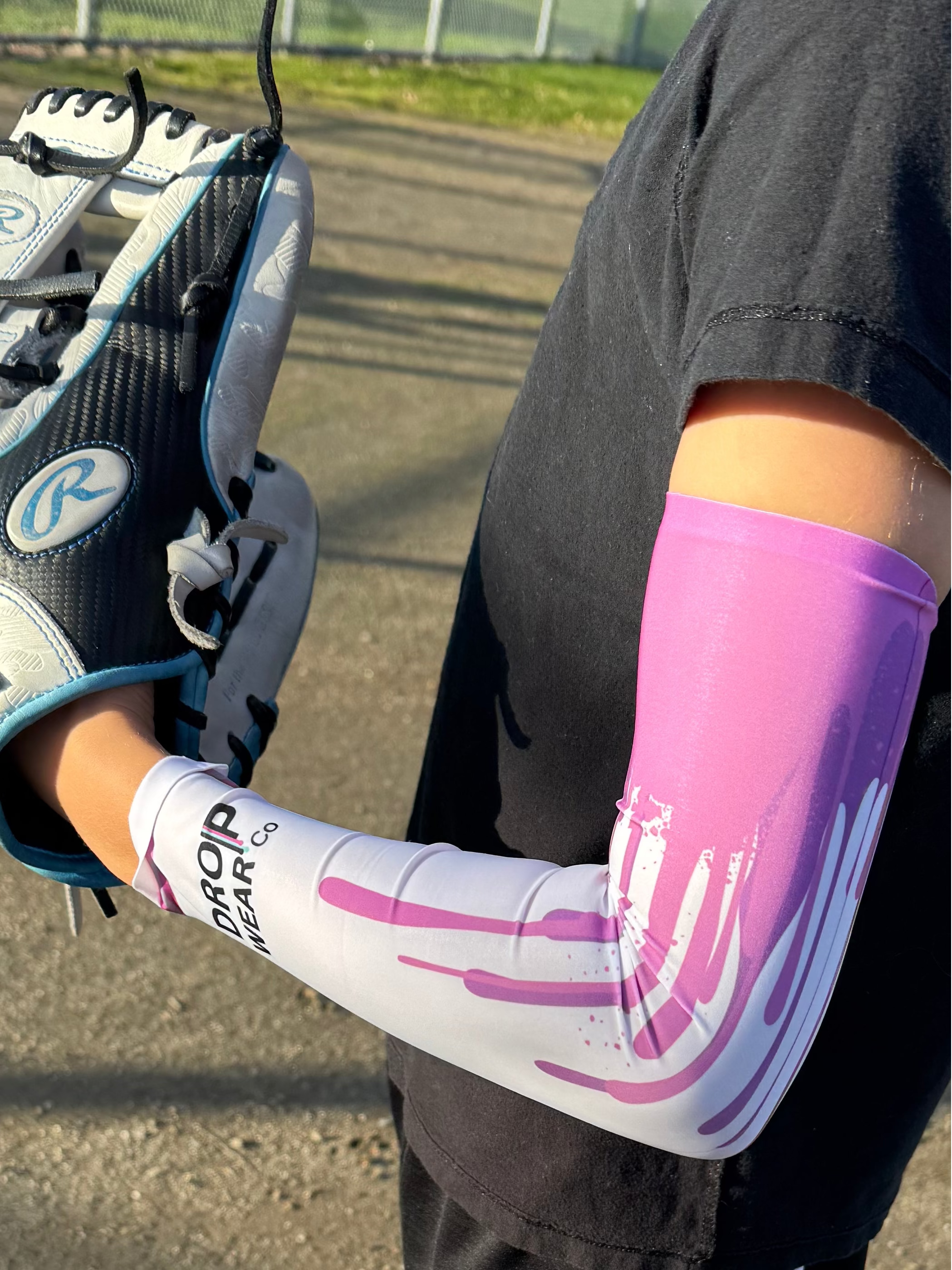 Person wearing a pink and white athletic arm sleeve and black sports outfit on a baseball field.